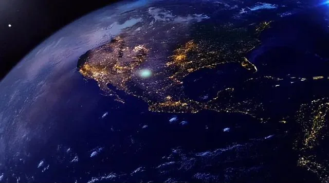 Earth seen from orbit at night, city lights glowing across the land and dark ocean spread between them.